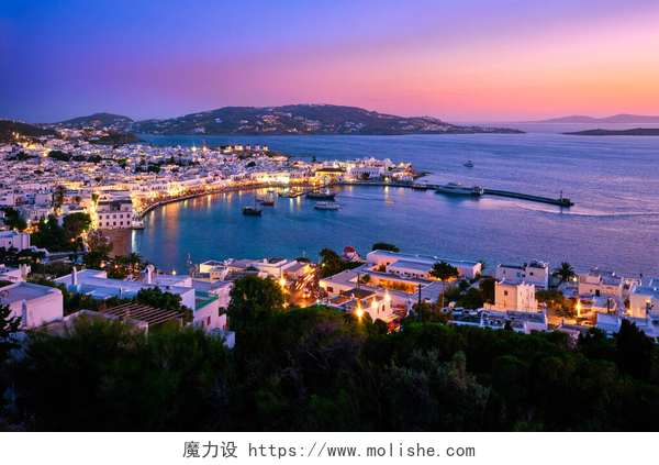 在日落的希腊上空和城市日落之后，在希腊的米科诺斯镇、 Cyclades镇、港口和港口、游轮、轮船、粉刷过的房屋上，景色多姿多彩。五彩缤纷的小镇灯火通明.